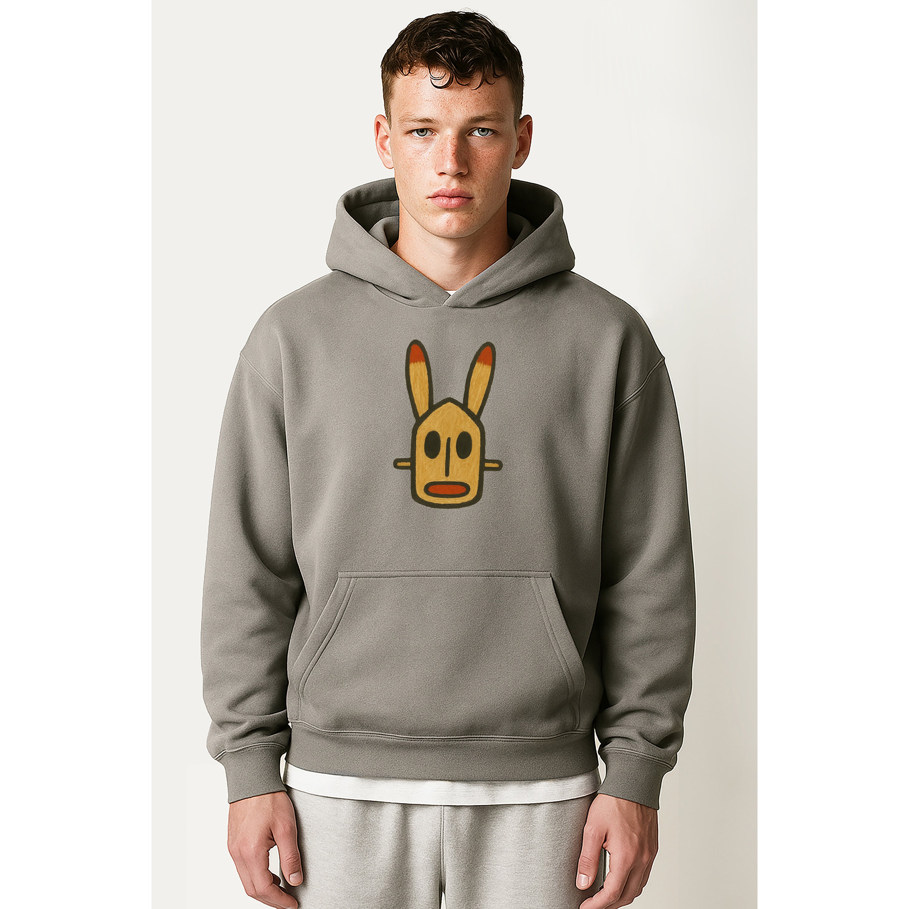 Man wears grey hoody with painted Mali dogon rabbit african mask at center chest on a solid white background
