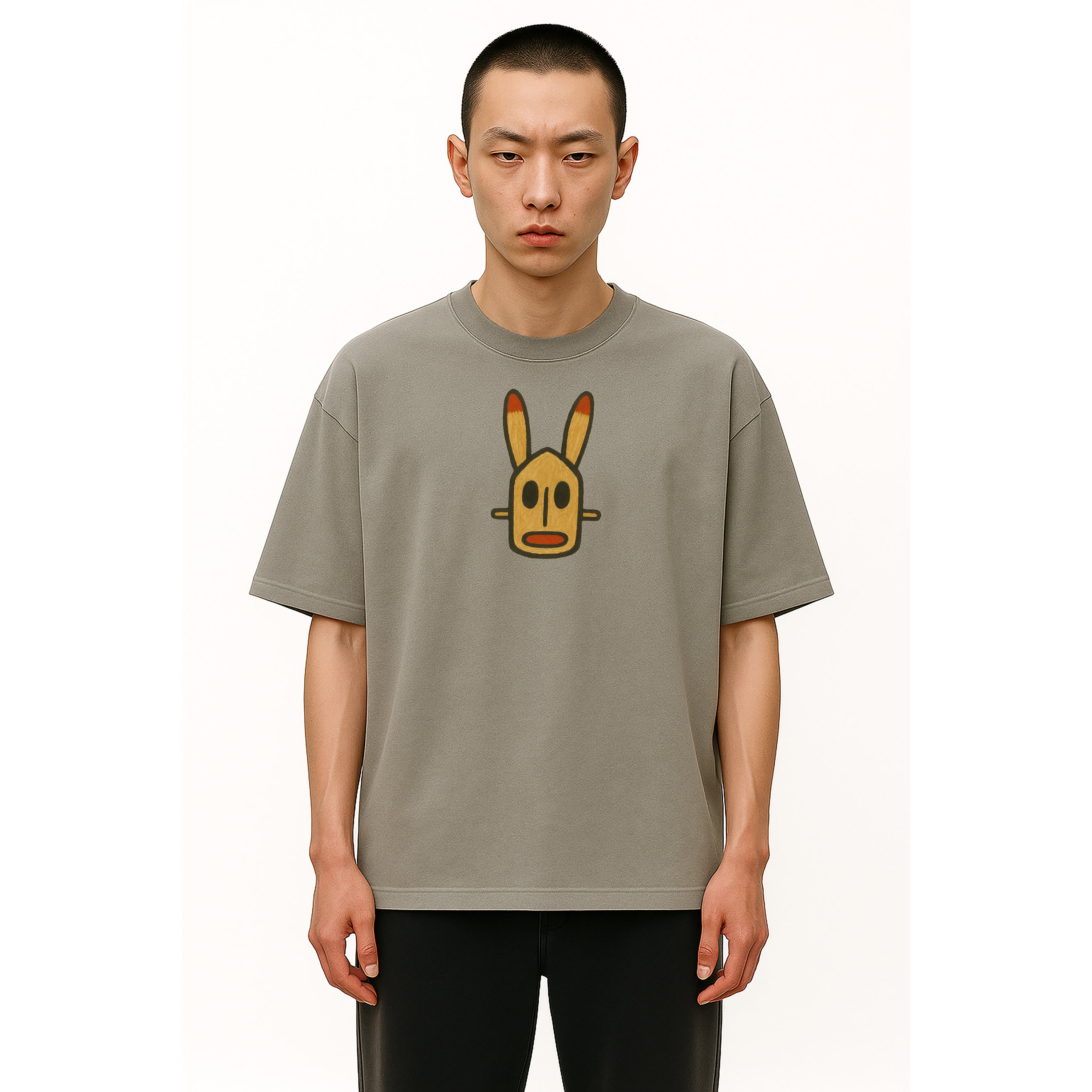 Man wears oversized heavyweight tee in grey with painted Dogon Mali graphic African Mask on solid background