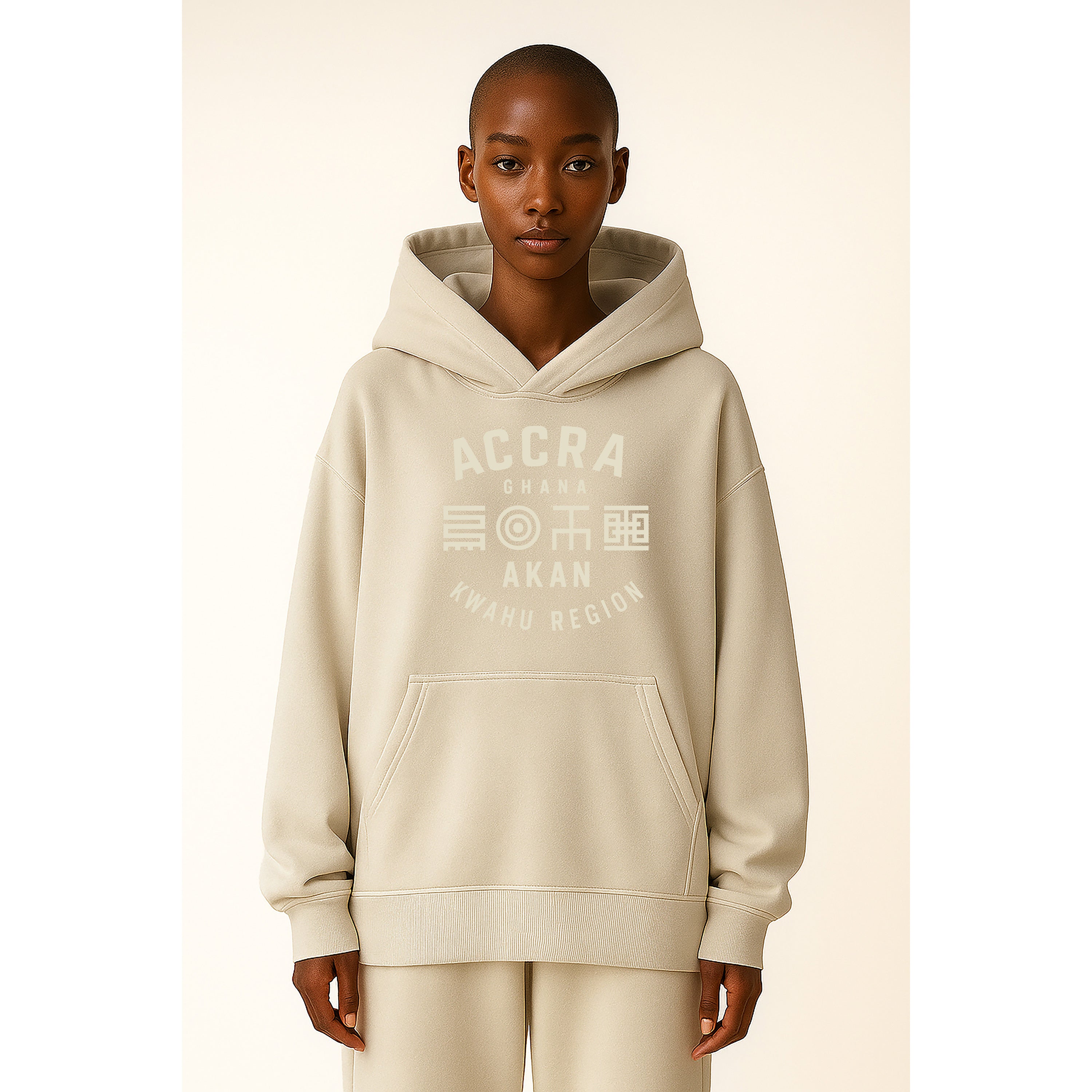 A model wears Ghana Akan Script Heavyweight Hoodie in Ash Grey with Stone DTG print featuring Adinkra-inspired symbols across the chest